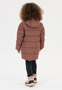 Brun puffjakke med hætte, med quiltet design og elastiske manchetter, parret med sorte leggings og pink støvler med pelsdetaljer.