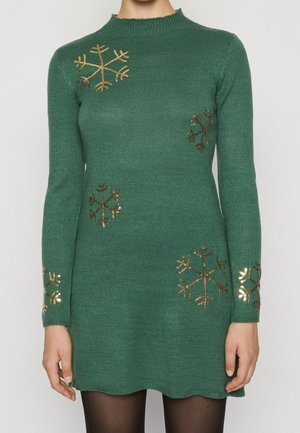 Green knit dress with gold sequin snowflake patterns on chest, sleeves, and skirt, worn with black tights.