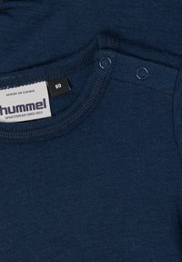 Navyblå stickad bomullsskjorta med rund halsringning, försedd med två tryckknappar på axeln och en etikett som visar storlek 80.