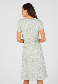Vestido floral en suave tela verde claro. Mangas cortas, escote redondo y silueta en A. Presenta pequeños patrones de flores blancas en toda su superficie.