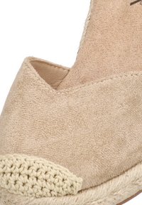 Sandalia de cuña de ante beige con una punta de yute trenzado, que presenta una forma redondeada y una textura suave, diseñada para ser llevada con el talón al descubierto.