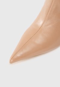 Nude kožená bota s špičatou špičkou, hladkým povrchem a minimálními švy. Špička je ostrá a celkový design je elegantní.
