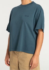 Bawełniana koszulka z krótkim rękawem w ciemnym niebiesko-zielonym kolorze z okrągłym dekoltem. Posiada subtelne logo na piersi oraz luźny, swobodny fason.