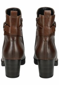 Bottines en cuir marron avec une finition texturée, des fermetures éclair sur les côtés et trois sangles superposées. Elles présentent un large talon noir.