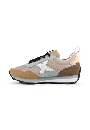 Zapatilla de corte bajo con bloques de color beige, marrón y gris, cordones negros, logo lateral blanco y suela blanca y negra.