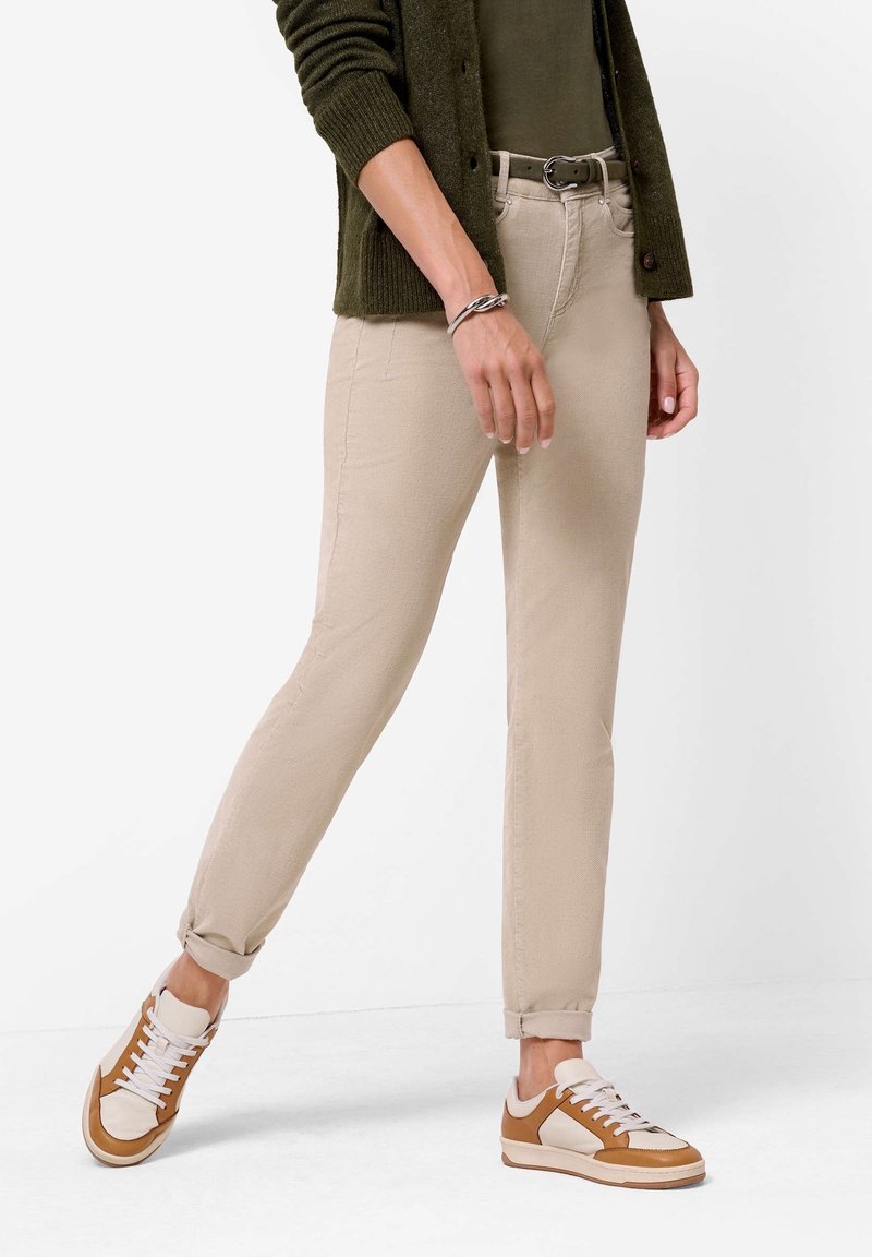 Beiga bomullsmixbyxor med slim fit, med uppvikta manschetter. Kombineras med bruna och vita sneakers och en mörkgrön cardigan. Bälte i midjan.