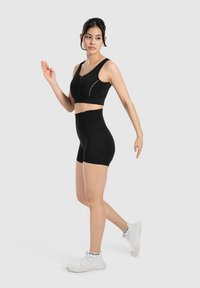 Zwarte sportbeha en hoge taille sportshorts in een getailleerd ontwerp. Bevat subtiele stiksels. Gemaakt in combinatie met witte sneakers.