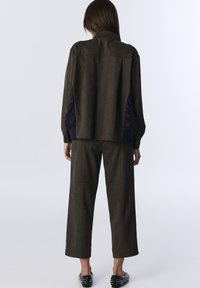 Oliwkowa kurtka z sztucznej zamszowej skóry z granatowymi akcentami, o luźnym kroju i długich rękawach, zestawiona z szerokimi spodniami w tym samym kolorze.