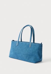 Modrý rifľový taška cez rameno s dvoma hornými rúčkami, obdĺžnikového tvaru, s minimálnym šitím a textúrovaným povrchom tkaniny.