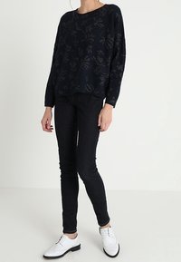 Marinblå stickad tröja med blommönster, avslappnad passform. Känns bra ihop med mörka skinny jeans och vita brogue-skor. Slät textur, avslappnad design.