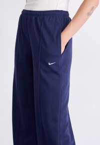Marineblauwe trainingsbroek van zacht materiaal, met een elastische tailleband, zijzakken en een klein wit Nike-logo op de dij.