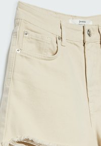 Beżowe szorty dżinsowe z wysokim stanem, z pięcioma kieszeniami i surowym wykończeniem hemu. Metalowe elementy z fakturowanym wykończeniem materiału.