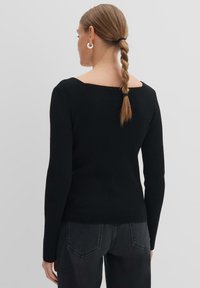 Schwarzer gerippter Pullover mit weitem quadratischem Ausschnitt und langen Ärmeln. Strukturiertes Gewebe, taillierte Silhouette, getragen mit dunklen Jeans. Einfaches Design.