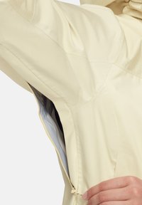 Helle gelbe wasserdichte Jacke mit einem Reißverschlussventil und verstellbarem Kordelzug. Glatte Textur und taillierte Passform mit geometrischen Schulterakzenten.