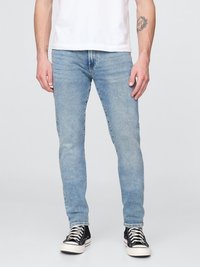 Jeans ajustados de denim en azul claro, con un acabado desgastado, cinco bolsillos y cremallera. Combinados con zapatillas negras de caña alta.