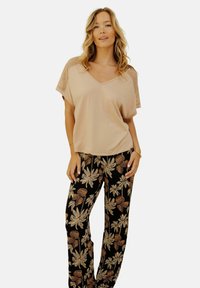 Haut beige à col en V avec des manches en maille à motifs, associé à un pantalon noir avec un design floral dans des tons beige et or.