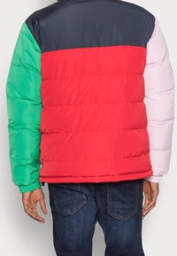 Kurtka puchowa w kolorze blokowym, z zielonymi, czerwonymi, granatowymi i różowymi sekcjami; posiada pikowaną teksturę i elastyczne mankiety; casualowy design.