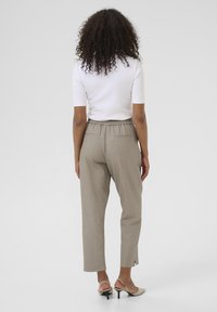 Pantalons texturés beige avec une coupe décontractée, dotés d'une taille élastiquée et d'ourlets fendus sur les côtés. Associés à un haut blanc ajusté et des chaussures beiges.