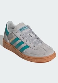 Adidas Handball Spezial sneakers in grijs suede met teal strepen, voorzien van een gumrubberen zool en gestikte details.
