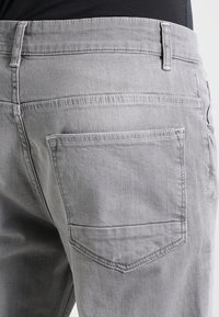 Jeans in denim grigio con un classico design a cinque tasche, con cuciture visibili e una texture morbida. La tasca posteriore ha un design a pattina appuntita.