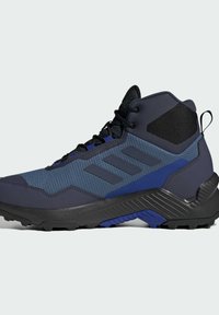 Högskurna vandringsskor i marinblått och svart. Har en texturerad ovandel, ett robust gummisula och tre randiga detaljer på sidan.