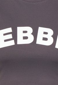 Gros plan d'un tissu foncé avec de grandes lettres blanches "EBB" imprimées en forme d'arche au centre.