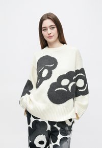 Beli ohlapen pulover s črnimi abstraktnimi cvetličnimi vzorci, rebrastim izrezom in manšetami. Ujet s črno-belimi hlačami s potiskom.