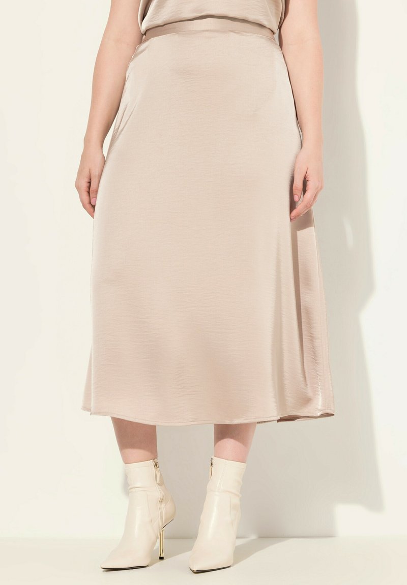 Beige, mid-lång kjol gjord av mjukt tyg, med en lätt lyster och subtil drapering, tillsammans med krämfärgade ankelstövlar med guldklack.