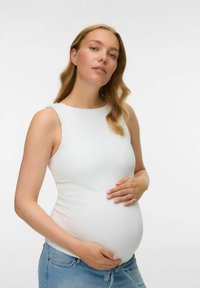 Vit åtsittande linne gjort av elastiskt material, bärs med blå jeans. Personen håller en synlig gravidmage.
