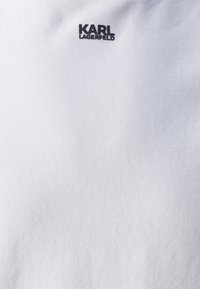 Camiseta blanca de algodón con una textura suave y un logo negro "Karl Lagerfeld" impreso en la parte superior del pecho. Cuello redondo, mangas cortas.