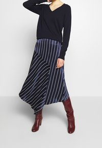 Czarny sweter z dekoltem w serek połączony z granatową spódnicą satynową w białe pionowe paski. Stylizację dopełniają bordowe kozaki za kolano.