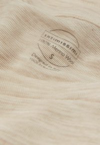 Tessuto in merino di un beige chiaro con una finitura testurizzata, dotato di etichette di cura stampate in inchiostro scuro, che indicano la taglia small e i dettagli del design.