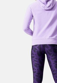 Sudadera lavanda con una textura suave y capucha, combinada con leggings negros y morados que presentan un patrón abstracto y paneles laterales elegantes.