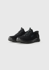 Pair of black Skechers slip-on athletic shoes with knit fabric, elastic laces, and thick rubber soles on white background.