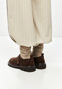 Beige stribede brede bukser over teksturerede beige sokker, kombineret med mørkebrune ruskindsko med tykke sorte såler.