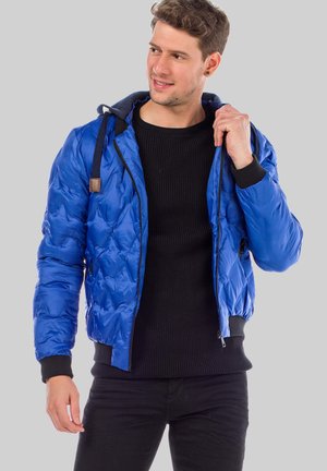 Blaue gepolsterte Jacke mit Kapuze, strukturiertem Äußeren und kontrastierenden schwarzen Rippbündchen. Verfügt über einen Reißverschluss und side Taschen.