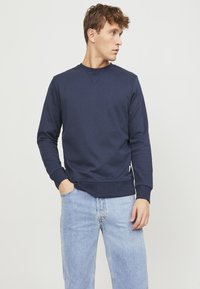 Marineblauwe sweatshirt van een zachte, gestructureerde stof met een ronde hals en geribde manchetten. Gecombineerd met lichtblauwe jeans, met een casual snit.