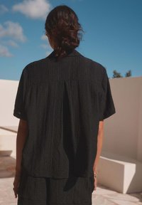Black short-sleeve shirt with a textured pattern and a back pleat, made from lightweight material, paired with a matching skirt.