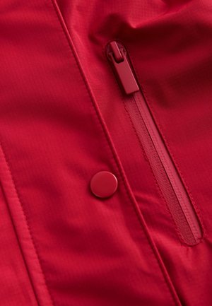 Raudonas audinio švarkas su paslėpta užtraukiama kišene ir apvaliu mygtuku. Tekstūra lygi su subtiliu blizgesiu.
