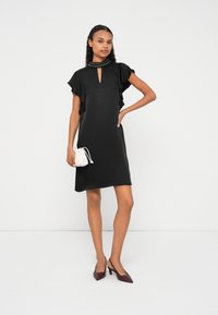 Čierne šaty s krátkymi volánikovými rukávmi, kľúčovým výstrihom a zdobeným golierom so cvočkami. Kombinované s bielou kabelkou a bordovými lodičkami.