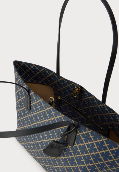 Sac fourre-tout avec un motif géométrique bleu et or, anses noires, ouverture supérieure, et une poche intérieure zippée. Fabriqué en matériau texturé.