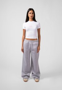 Hvit cropped t-skjorte med rosa logo, sammen med grå oversized joggebukser. Fottøyet har beige detaljer og en beige såle. Enkel, avslappet passform.