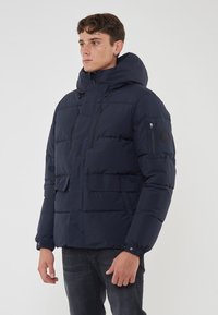 Giubbotto imbottito blu marino con cappuccio, caratterizzato da un design trapuntato, tasche con zip e polsini elasticizzati. Realizzato in materiale resistente all'acqua.