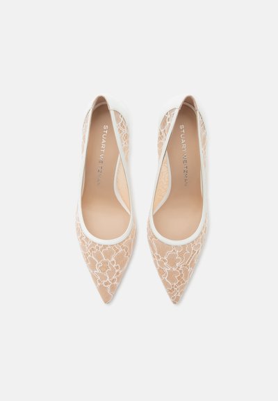 Paire de ballerines beiges à bout pointu avec overlay en dentelle florale blanche et bordure, affichant le nom de la marque à l'intérieur de chaque chaussure.