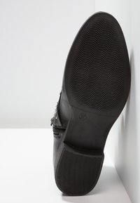 Sort ankelstøvle med tekstureret gummisål, lynlås og sølvnitter langs siden. Størrelse 37 markeret på sålen.