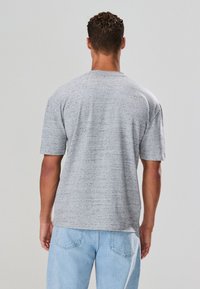 Grijs T-shirt met korte mouwen en een gestructureerd, gespetterd patroon. Rondhalzend ontwerp met een losse pasvorm, gecombineerd met lichtblauwe spijkerbroek.