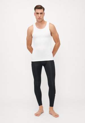 Weißes ärmelloses Tanktop, das mit schwarzen Leggings getragen wird. Das Tanktop ist glatt und figurbetont; die Leggings sind dehnbar und elegant, mit einem kleinen Logo.