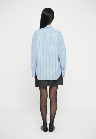 Camicetta a righe blu chiaro con maniche lunghe, orlo curvo e polsini con bottoni, abbinata a una gonna di jeans scura e collant neri.