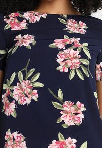 Navy floral top with short sleeves, featuring pink and green floral patterns. Smooth fabric with a slight sheen and subtle pleating detail.