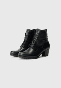Bottes noires en cuir à la cheville avec un bout rond, un système de lacets et un petit talon carré. Texture lisse avec des détails de surpiqûres bien visibles.